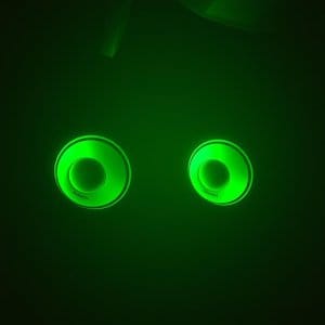 Glowing green speaker lights in a dark room, resembling eyes.